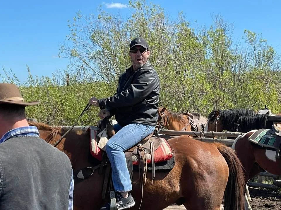Larry laughing on horseback in a leather jacket at a trail-ride corral