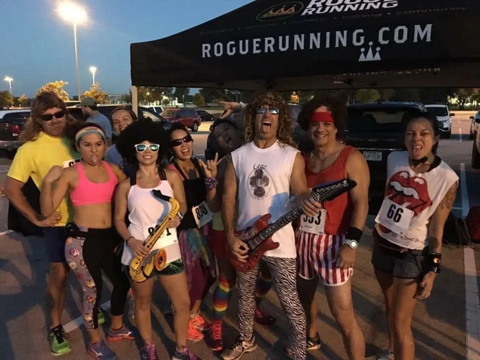 Larry in a curly wig with an inflatable guitar, the Sparks around him in rock costumes under the Rogue Running tent